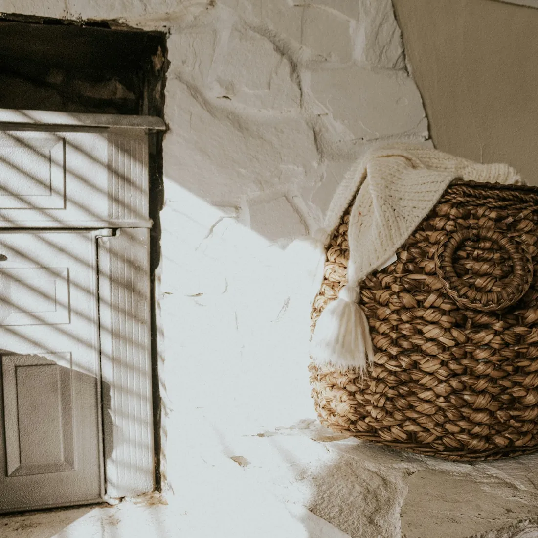 Cesta de fibra vegetal trenzada apoyada junto a un muro encalado, con la trama de la pared del cesto a la vista
